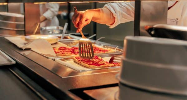 Eine Mensa-Mitarbeiterin mit frischer Pizza in der Speisenausgabe-Theke.