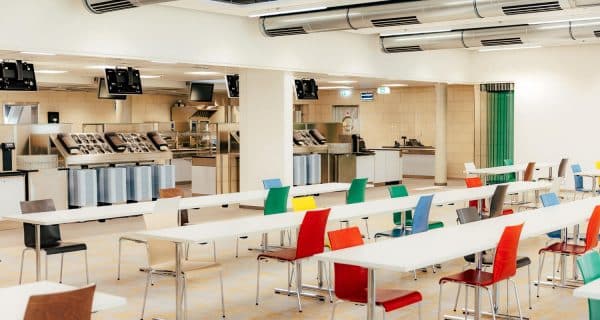 Innenansicht der Mensa US mit langen Tischreihen und bunten Stühlen.