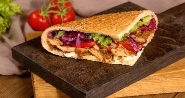 Ein Döner mit Fleisch und Salat auf einem Holzbrett.