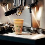 Ein Becher wird an einer Siebträgermaschine mit Kaffee befüllt.